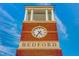 Low angle close-up of the brick Bedford clock tower displaying a large clock face against a partly cloudy sky at 10603 Friendly Neighbor Ln, Raleigh, NC 27614