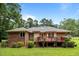Green lawn and trees highlight the back and side of the brick home with a red wooden deck at 143 Cedarwood Dr, Henderson, NC 27536