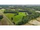 Wide aerial view of verdant property featuring a red barn, surrounded by green trees and open fields at 1167 John D Winstead Rd, Roxboro, NC 27574