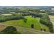 Expansive aerial shot showcases a red barn amidst green pastures, forests, and a neighboring road at 1167 John D Winstead Rd, Roxboro, NC 27574