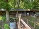 Rustic outbuildings and chicken coop on a wooded property with a vintage water barrel and fencing at 1167 John D Winstead Rd, Roxboro, NC 27574