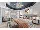 Staged primary bedroom featuring a tray ceiling, ceiling fan, and two large windows at 130 Virginia Water Dr, Rolesville, NC 27571