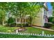 A view of the home showcasing its yellow siding, covered porch, tidy landscaping, and white picket fence at 4001 Falls River Ave, Raleigh, NC 27614