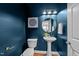 Stylish powder room with blue walls, pedestal sink, gold accents, and decorative round mirror at 904 Pirouette Ct, Raleigh, NC 27606