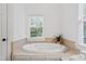 Bright bathroom showcasing an elegant soaking tub with tile surround and a view of the outdoor scenery at 118 Killingsworth Dr, Cary, NC 27518