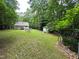 Spacious backyard featuring a lush lawn, trees, house, and a small outbuilding on the wooded lot at 8116 Reynard Rd, Chapel Hill, NC 27516
