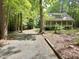 Green home with covered front porch is surrounded by trees and lush foliage, sitting on a gravel driveway at 8116 Reynard Rd, Chapel Hill, NC 27516