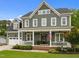 Traditional two-story home with a covered front porch, American flag, green siding, and manicured lawn at 821 Rambling Oaks Ln, Holly Springs, NC 27540