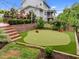 Backyard putting green with lush landscaping, string lights, and an outdoor fireplace at 821 Rambling Oaks Ln, Holly Springs, NC 27540