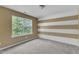 Cozy bedroom with a large window allowing natural light, carpet floors, and unique striped wall at 211 Westgrove Ct, Durham, NC 27703