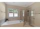 Bright bathroom featuring a soaking tub with tile surround, a glass shower, and a large window at 10809 Grassy Creek Pl, Raleigh, NC 27614
