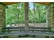 Covered porch showcases a wooden bench and stone pillar, providing a serene view of the lush, wooded landscape at 110 Wolfs Trl, Chapel Hill, NC 27516