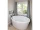 Elegant white soaking tub beside a window with chrome plumbing fixtures and gray curtains at 9136 Palm Bay Cir, Raleigh, NC 27617