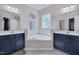Bathroom with dual vanities, corner soaking tub, neutral tile, and natural light at 62 Mountain Laurel Ln, Four Oaks, NC 27524