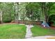 Spacious backyard with mature trees, green grass, stepping stone path, and wooded area at 709 Bonhurst Dr, Holly Springs, NC 27540