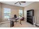 Well-lit home office with dual windows, ceiling fan, modern desk setup, and ample bookshelf space at 2122 Aventon Ln, Morrisville, NC 27560