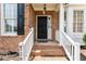 Inviting front porch with a black front door, classic white railings, and brick steps at 712 Brittley Way, Apex, NC 27502