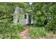 Charming white shed with a gray door, surrounded by lush greenery and a stone pathway at 1004 E Willowbrook Dr, Burlington, NC 27215