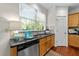 Kitchen featuring a stainless steel dishwasher, black countertops, natural wood cabinets, and a large window at 5545 Moneta Ln, Apex, NC 27539
