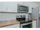 Close-up of the kitchen range with wood counters, white cabinets, stainless steel appliances, and subway tile backsplash at 169 Forest Dr, Graham, NC 27253