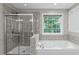 Bright bathroom featuring a glass-enclosed shower, large soaking tub, and a window overlooking lush greenery at 101 Quarryrock Rd, Holly Springs, NC 27540