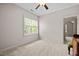Neutral bedroom featuring light walls and carpet, window, ceiling fan, and doorway leading to another room at 12216 Kyle Abbey Ln, Raleigh, NC 27613