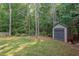 View of the backyard with a storage shed, mature trees, and a lush green lawn at 1612 Old Bramble Ln, Fuquay Varina, NC 27526