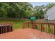 Large backyard with a brown deck, lush green grass, playground, and privacy fence at 8201 Ivymount Way, Raleigh, NC 27613