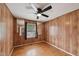A bedroom featuring wood-paneled walls, a ceiling fan with a light fixture, and a window with dark curtains at 555 Dacian Rd, Raleigh, NC 27610