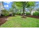 Landscaped backyard featuring green grass, mature trees, mulched beds, and a small deck at 106 Roundtop Rd, Cary, NC 27519