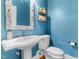 This bathroom features a pedestal sink, wall-mounted mirror and shelves, and blue walls at 6005 Carlyle Dr, Raleigh, NC 27614