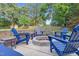 Outdoor fire pit area with blue Adirondack chairs on a concrete patio, surrounded by a stone retaining wall and greenery at 3713 Highland Creek Dr, Apex, NC 27539
