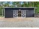 Charming black barn featuring white doors and a metal roof, surrounded by gravel and trees at 4737 Uzzle Rd, Rougemont, NC 27572