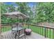 A wooden deck includes an umbrella, table and chairs surrounded by a green grass and tall trees at 7613 Percy Ct, Raleigh, NC 27613
