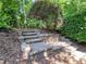 Lush backyard with stone steps and retaining wall featuring colorful landscaping and mature trees, ideal for outdoor enjoyment at 224 Midden Way, Holly Springs, NC 27540