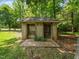 Utility shed with dual access doors, concrete foundation, and brick wall under mature shade trees at 8917 Thompson Mill Rd, Wake Forest, NC 27587