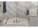 Close up of a corner soaking tub in an elegant bathroom with patterned wallpaper and neutral tile at 2813 Market Bridge Ln # 104, Raleigh, NC 27608