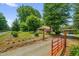 A beautiful tree-lined property featuring a charming brick home, green lawn, and open red gate entry at 3315 Mebane Oaks Rd, Mebane, NC 27302