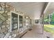 Covered stone porch featuring stamped concrete, exterior lighting, and access to a serene outdoor setting surrounded by greenery at 7849 Circle L Trl, Rougemont, NC 27572