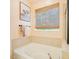 Soaking tub with tile surround beneath a bamboo shade window in a sun-filled bathroom at 903 Grace Point Rd, Morrisville, NC 27560
