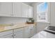 This laundry room offers ample storage with white cabinets, a utility sink, and a bright window at 113 Market Cross Ct, Holly Springs, NC 27540