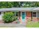 Close-up of a ranch home's brick facade and teal front door, complemented by verdant landscaping at 3216 Idlewood Village Dr, Raleigh, NC 27610