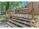 Backyard with a wood deck and stairs leading up to the brick home and door. Large trees provide ample shade at 3221 Ward Rd, Raleigh, NC 27604