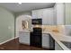 Well-equipped kitchen featuring white cabinets, black appliances, and hardwood floors, with a view to the stairway at 100 Tobacco Leaf Ln, Apex, NC 27502