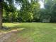 Large, green backyard featuring mature trees and an empty fire pit at 2037 Swepsonville Rd, Graham, NC 27253