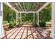 Elegant pergola with a brick patio, lush plants, seating, and natural backyard views at 2283 Mays Chapel Rd, Sanford, NC 27330