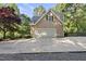 View of tan house with an attached garage and concrete driveway surrounded by lush greenery and trees at 3412 Paddock Cir, Raleigh, NC 27613