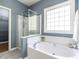 Bathroom features a soaking tub with a shower, grey tile flooring, and a large window at 3709 Andoversford Ct, Wake Forest, NC 27587