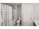 This bathroom includes a toilet, a shower-tub combo with white-gray shower curtain, and a door to the side at 7873 Cape Charles Dr, Raleigh, NC 27617
