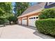 Three-car garage with brick exterior and white doors, surrounded by lush greenery and mature trees at 104 San Sophia Dr, Chapel Hill, NC 27514